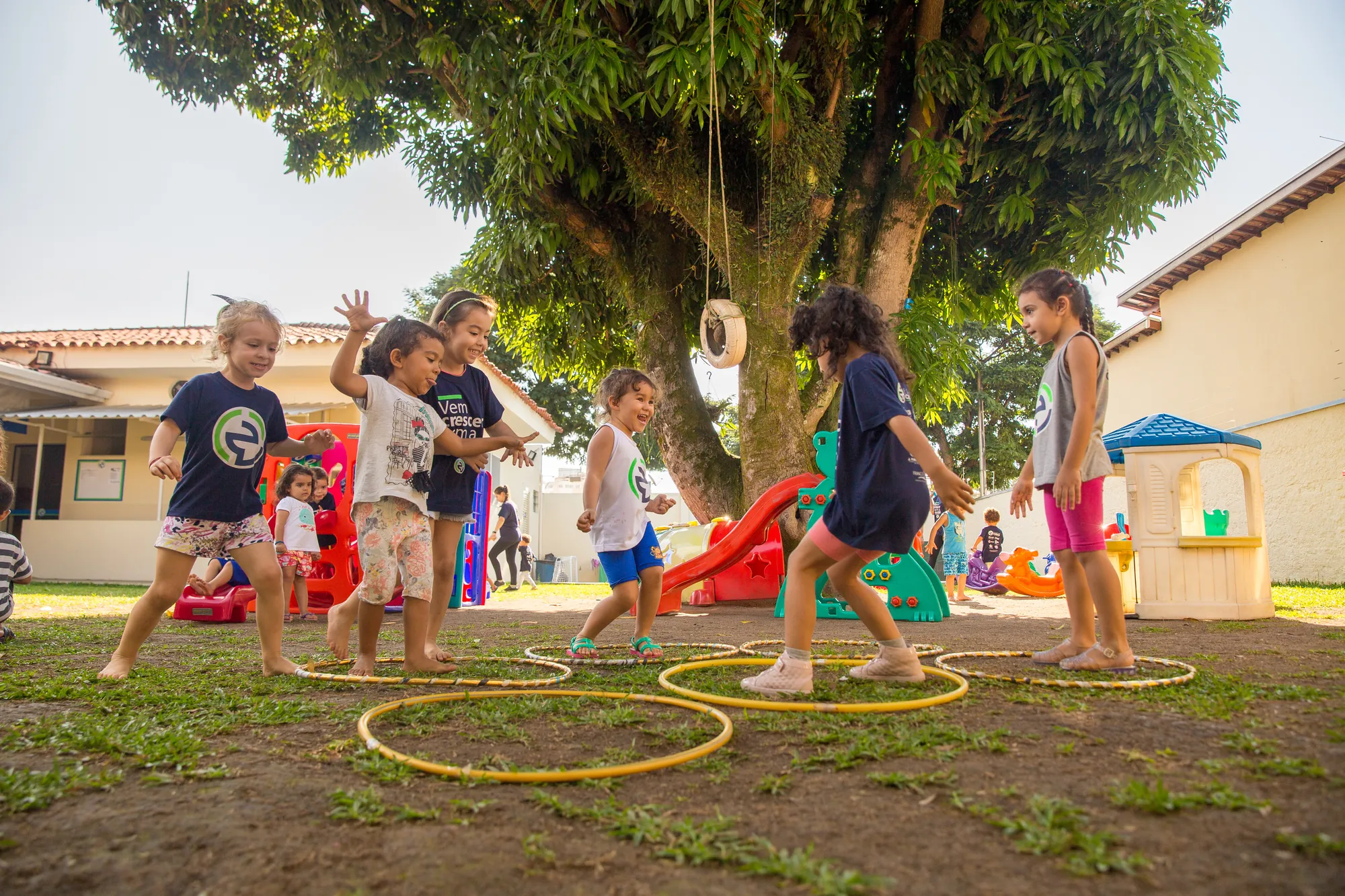 Crianças brincando com bambolês embaixo da árvore do pátio
