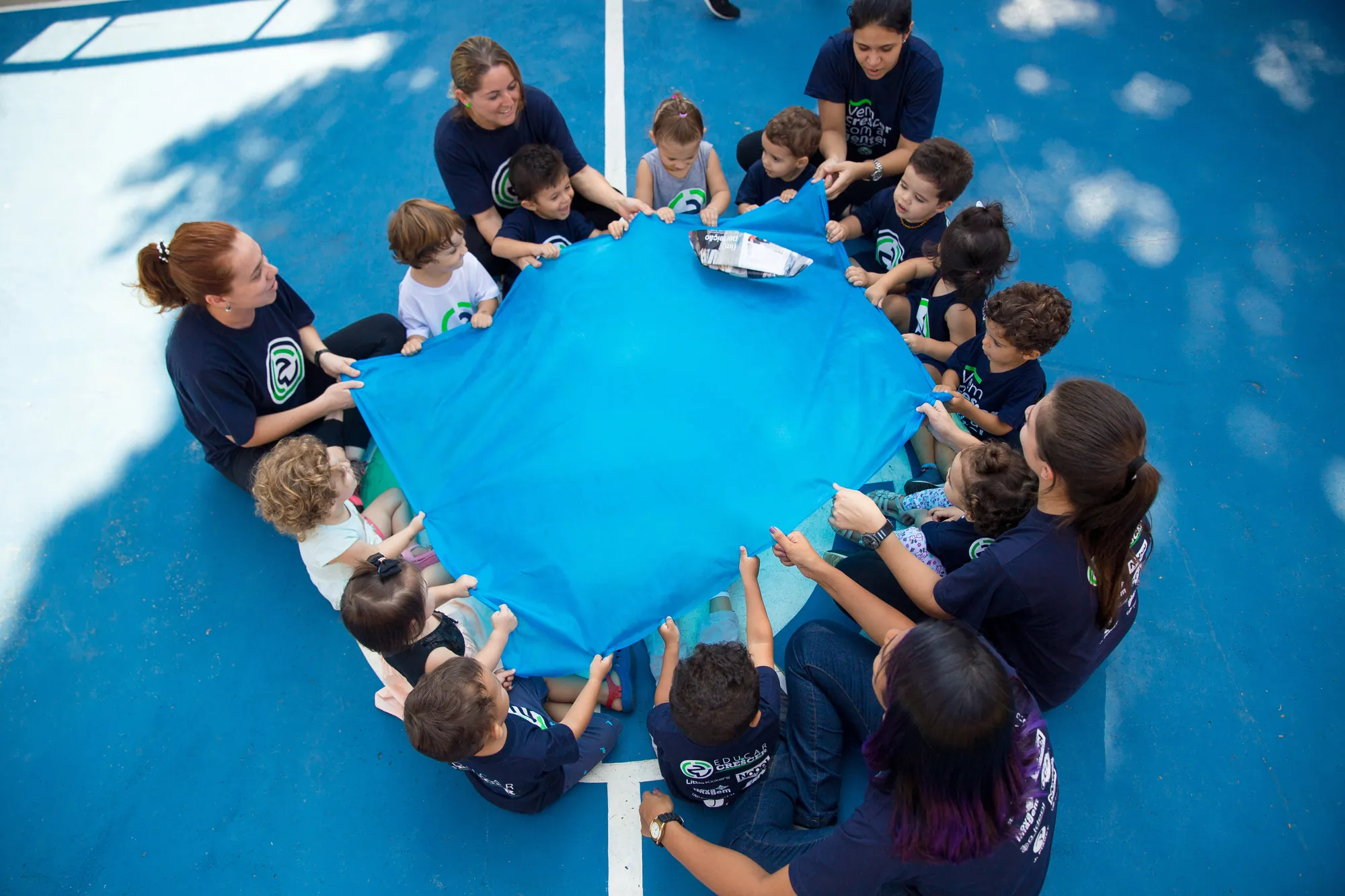 Crianças e educadoras brincando com o paraquedas na quadra